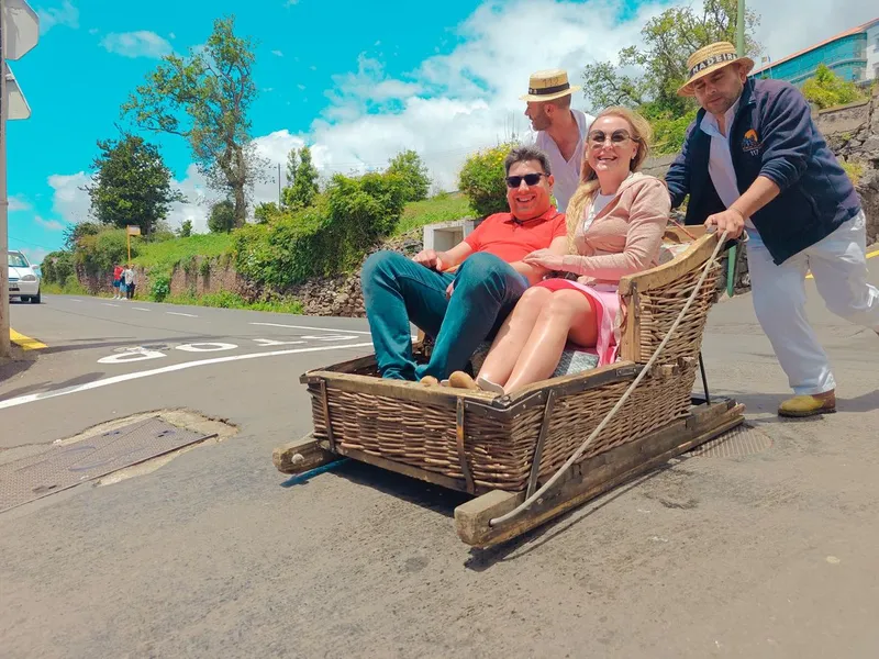 Two toboggan runners steering a wicker basket sledge down a paved street from Monte on a Funchal Monte toboggan tour by tuk-tuk in Monte, Madeira
