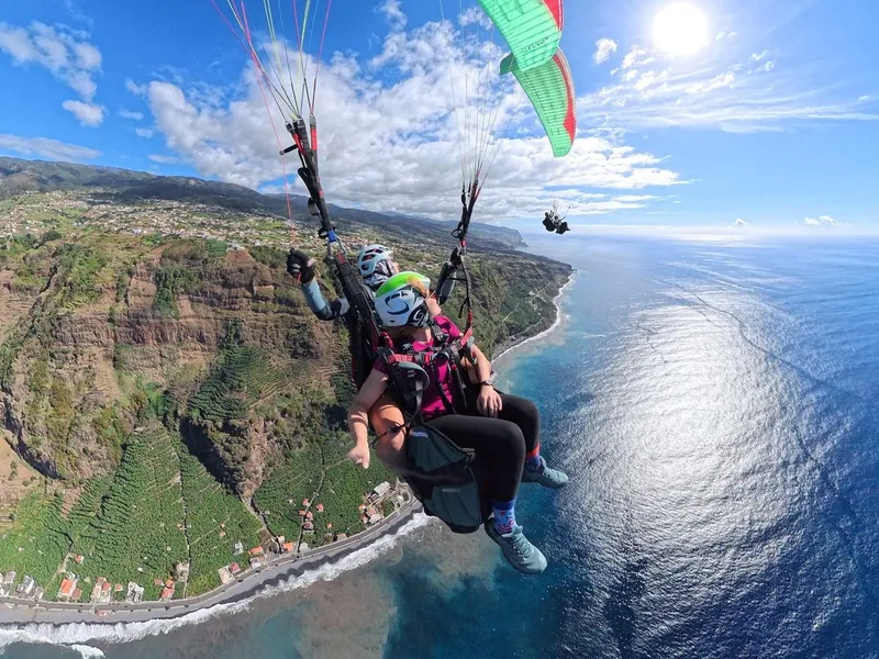 A tandem paraglider soaring above the green cliffs of Madeira's west coast on a Tandem Paragliding Flight in Canhas, Madeira